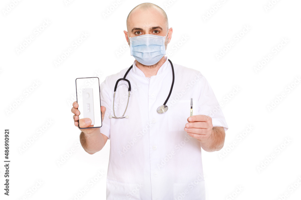 Middle-aged doctor in white robe with stethoscope on his neck on a white background holding a phone with a positive test and a syringe with the inscription covid Middle-aged doctor in white robe with stethoscope on his neck on a white background holding a phone with a positive test and a syringe with the inscription covid