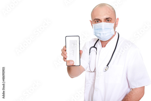 Middle-aged doctor in white robe with stethoscope around his neck on a white background holding a phone with a positive test