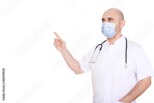 Middle-aged doctor in a white robe and with a stethoscope around his neck on a white background pointing to the left