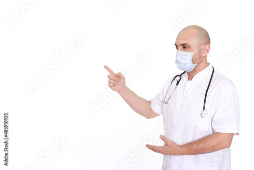 Middle-aged doctor in a white robe and with a stethoscope around his neck on a white background pointing to the left