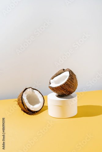 Two halves of coconut and a jar of cosmetics on a yellow and gray background. © Marevgenna