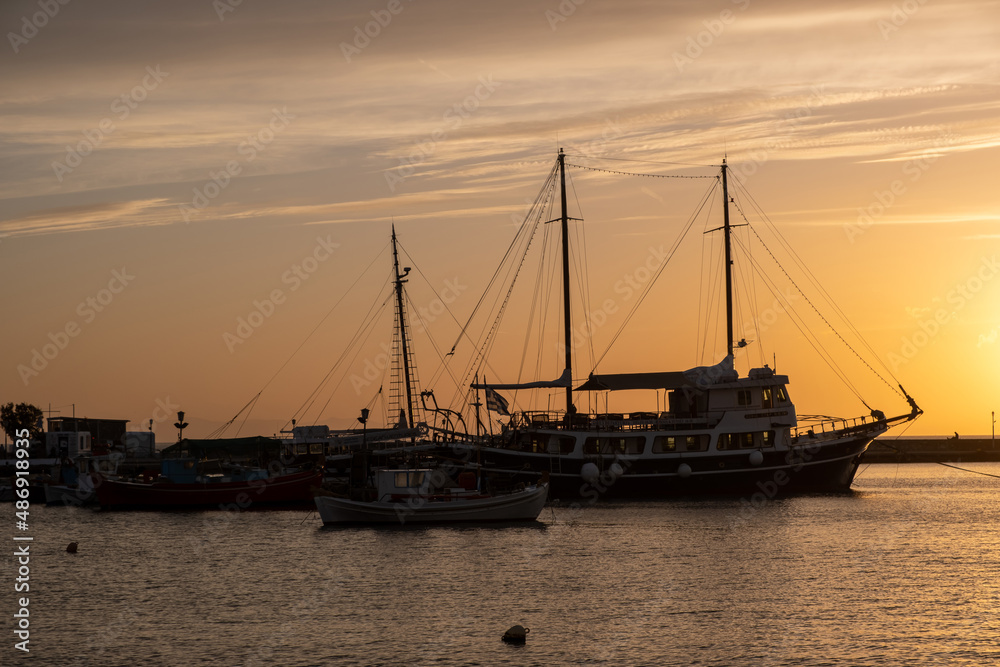 Sunset over Mykonos island, Cyclades, Greece. Moored ship at port, beacon orange sky sparkle sea.
