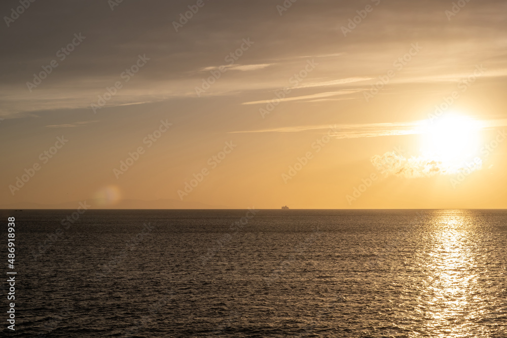 Sunset over calm sea, golden sun colors the sky orange, yellow and make sea sparkle.