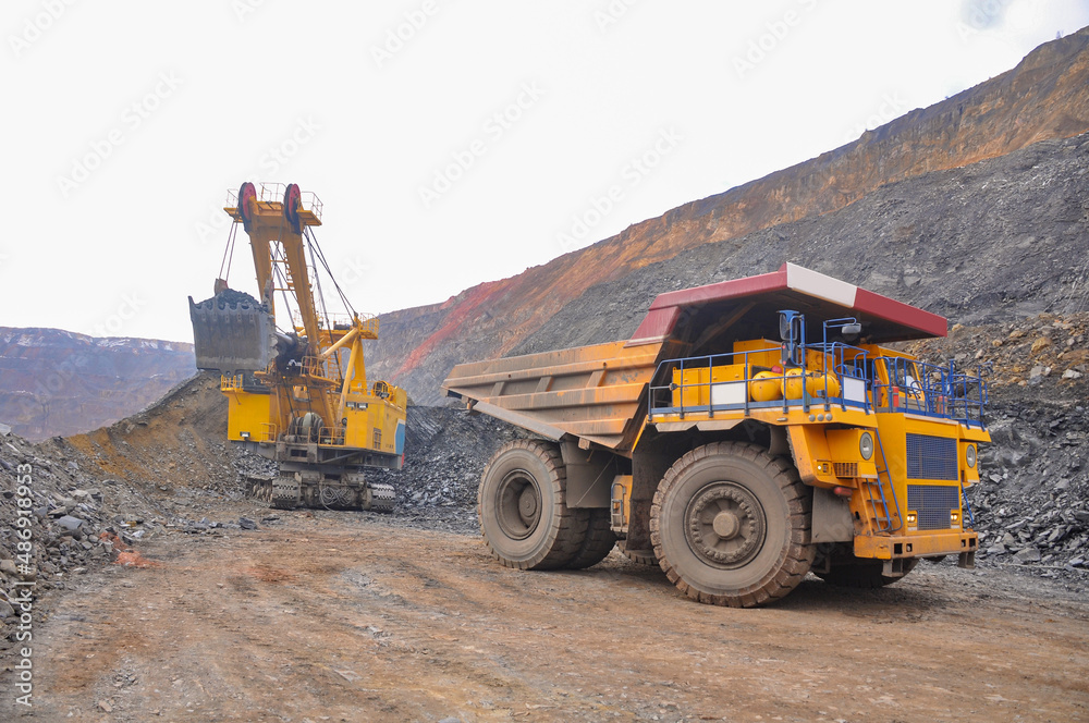 A dump truck drives up to an excavator for loading rock mass from an iron ore quarry