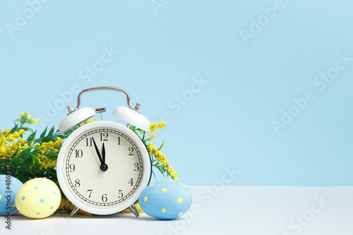 Easter concept. Alarm clock eggs flowering branch on a blue background. copy space.