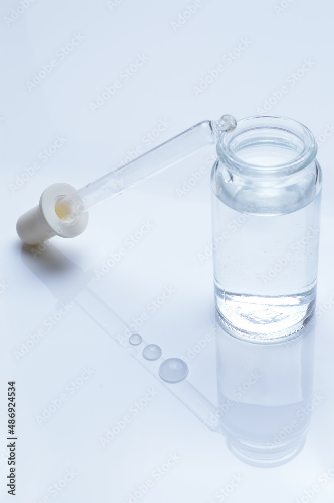 glass transparent jar and a cosmetic pipette with liquid droplets on a white background. glass transparent jar and a cosmetic pipette with liquid droplets on a white background.