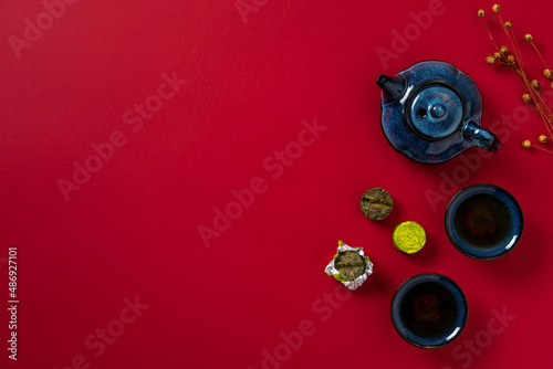 Blue teapot, cup of tea and tea leaves on red background. Hot herbal tea is in the teapot on the table. Copy space.