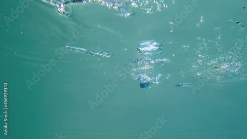 Discarded plastic bottles and cups drifting underwater in blue water column with glare. Plastic garbage environmental pollution problem in seas and ocean. Ecological catastrophy. Close up, slow motion photo