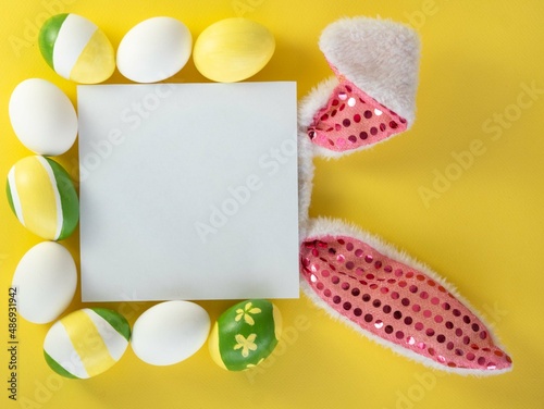 Bunny ears, a white square with space for text and painted flowered striped Easter eggs on yellow. Easter card concept.