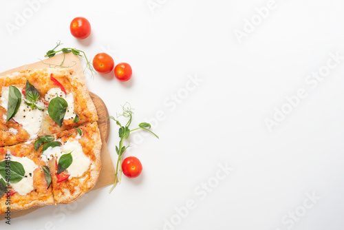 Close-up of a delicious Roman pizza with vegetables on a wooden board. white background around ripe red tomatoes and micro-greens lie nearby. Traditional Italian food. Top view, flat lay, copy space photo
