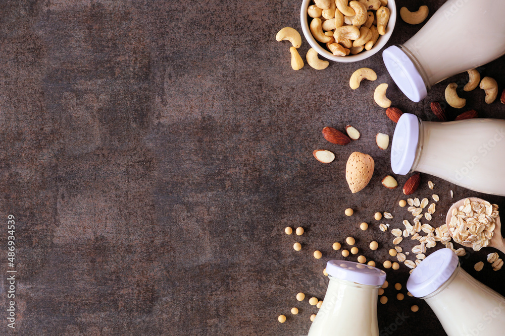 Vegan plant based non dairy milk top border. Selection in milk bottles with scattered ingredients. Overhead view over a brown stone background with copy space. Vegan plant based non dairy milk top border. Selection in milk bottles with scattered ingredients. Overhead view over a brown stone background with copy space.