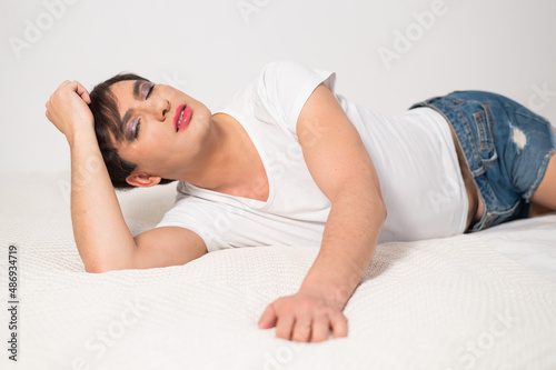 Caucasian transgender man lies on gay bed. Outdoor gay posing in the bedroom.