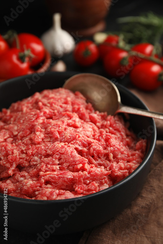 Fresh minced meat and spoon in bowl on table, closeup