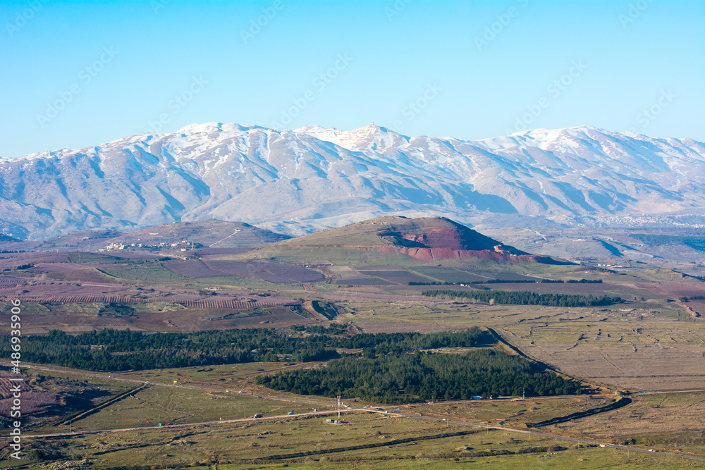 Mount Hermon in Israel in the winter with the Golan Heights beneath with roads and green fields.