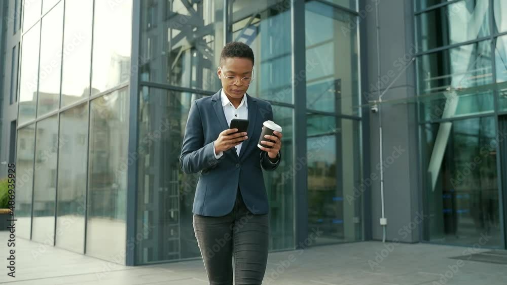 business black woman walking on city street downtown with mobile phone and cup coffee. African American female employee entrepreneur uses a smartphone on urban background. confident office worker business black woman walking on city street downtown with mobile phone and cup coffee. African American female employee entrepreneur uses a smartphone on urban background. confident office worker