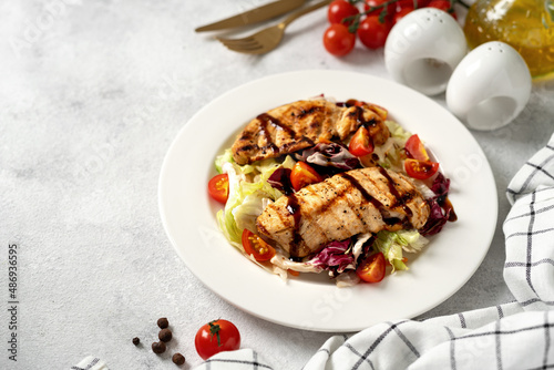 Grilled chicken fillet with vegetables in a white plate on a light gray culinary background. Dietary poultry breast on the kitchen table closeup