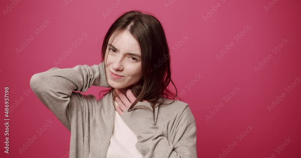 Unhealthy young woman touches her neck, having discomfort or painful sensation and back pain, sad sad girl suffering from angina pectoris, sore throat isolated on a pink background studio