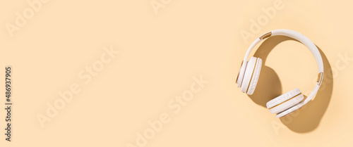 Wireless headphones on a beige background. Flat lay, top view. Banner.