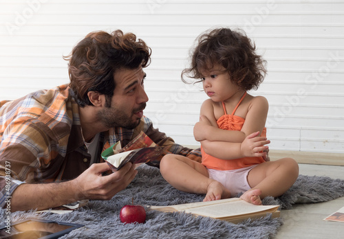 Father and daughter spending time together.  Dad teaches cute littel toddler girl after she tore page of book.