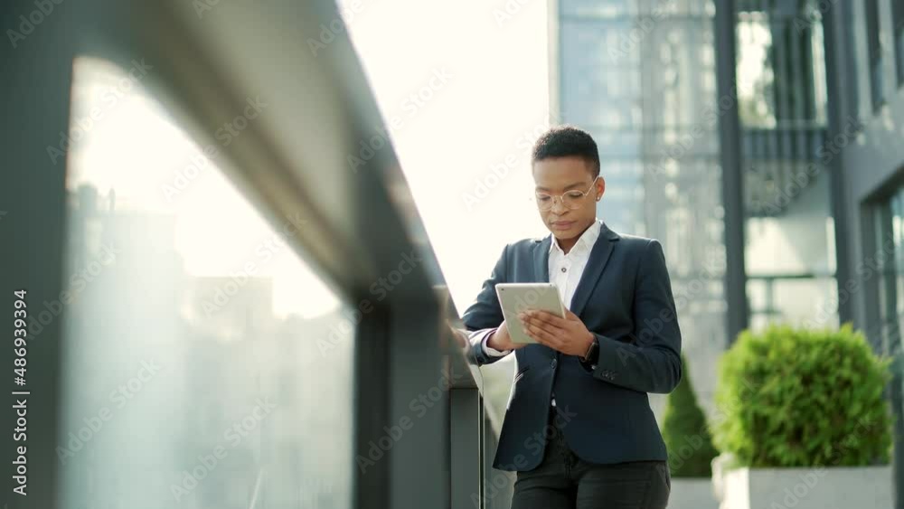 african american businesswoman employee in formal business suit standing working with tablet on background modern office building outside. Woman using smartphone or mobile phone outdoors city street african american businesswoman employee in formal business suit standing working with tablet on background modern office building outside. Woman using smartphone or mobile phone outdoors city street