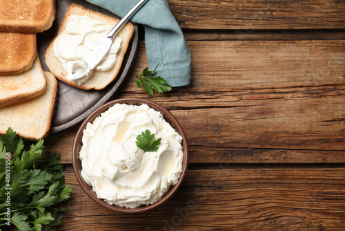 Toasted bread and delicious cream cheese with parsley on wooden table, flat lay. Space for text