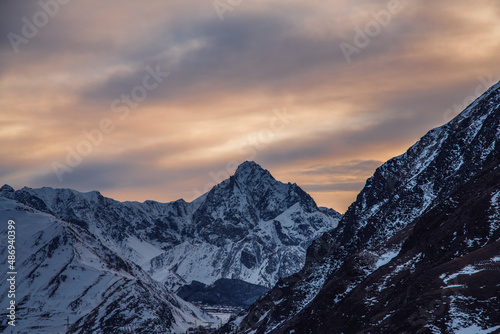 Beautiful winter mountain landscape at the sunrise with dramatics clouds. High snow covered mountains in the fog. 