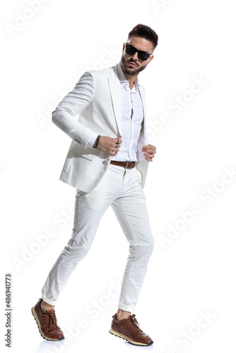 cool young businessman with sunglasses adjusting suit and walking