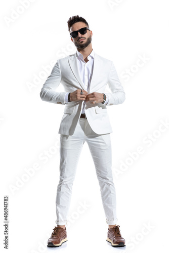 full body picture of cool man buttoning suit and posing in a fashion light