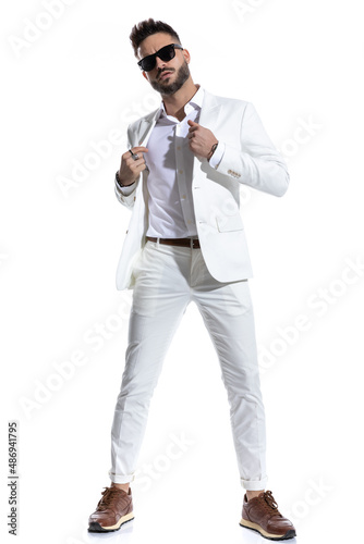 confident bearded guy with sunglasses adjusting suit and posing