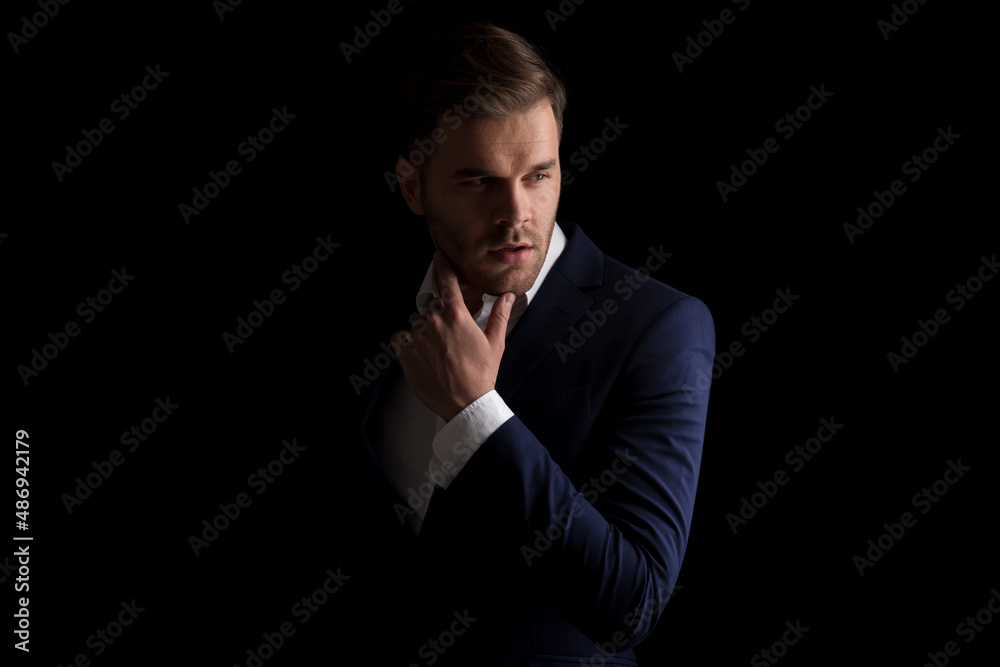 sexy businessman in suit holding hand to neck and looking to side