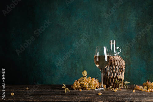 A glass of homemade white wine with grapes and a bottle on a rustic wooden table