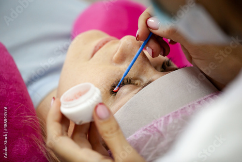 A girl makes the procedure for extending eyelashes during a pandemic  a master with tools in her hands