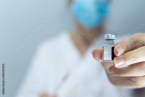 Close-up nurse in mask holds bottle with vaccine medication for coronavirus cure, health care and vaccination concept
