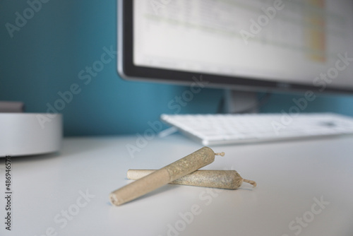 Winnipeg, Manitoba, Canada - February 12, 2022: Close-up of Pre Rolled Joints with an Unfocused Computer in the Background. photo