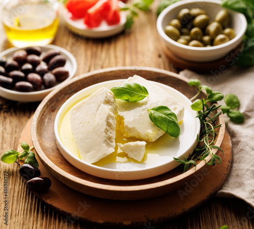 Feta cheese with the addition of olive oil and fresh basil on a ceramic plate, close up view. Traditional Greek product