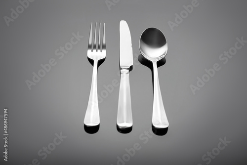 Cutlery set - fork, table knife and table spoon on a gray glossy background