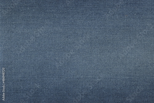 The texture of natural blue denim fabric with scuffs. Rough cotton. Abstract background of natural denim.