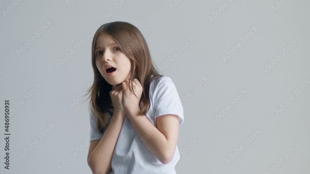 A blonde teen girl in a white T-shirt is frightened and afraid against the background of a white wall A blonde teen girl in a white T-shirt is frightened and afraid against the background of a white wall
