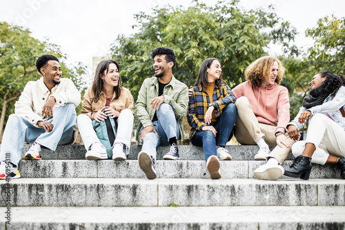 Group of happy young friends laughing outdoors - Hipster people having fun together while sitting on stairs in city