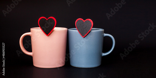 Two cups pink and gray color for coffee, stand on a black background. Place for text. Banner. Coffee day. Valentine's Day. Close-up cups. Minimalism with coffee. Breakfast. Mockup. Close up