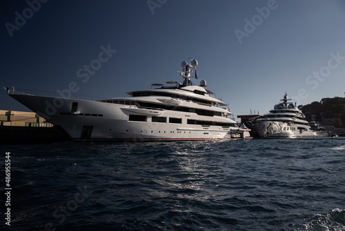 Two huge yacht in port of Monaco at sunset, glossy board of the motor boat, the chrome plated handrail, megayacht is moored in marina, sun reflection on glossy board, mountain is on background © Vladimir Drozdin