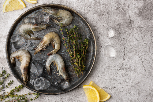 Plate with shrimps, raw prawns with lemon slices, ice cubes and thyme.