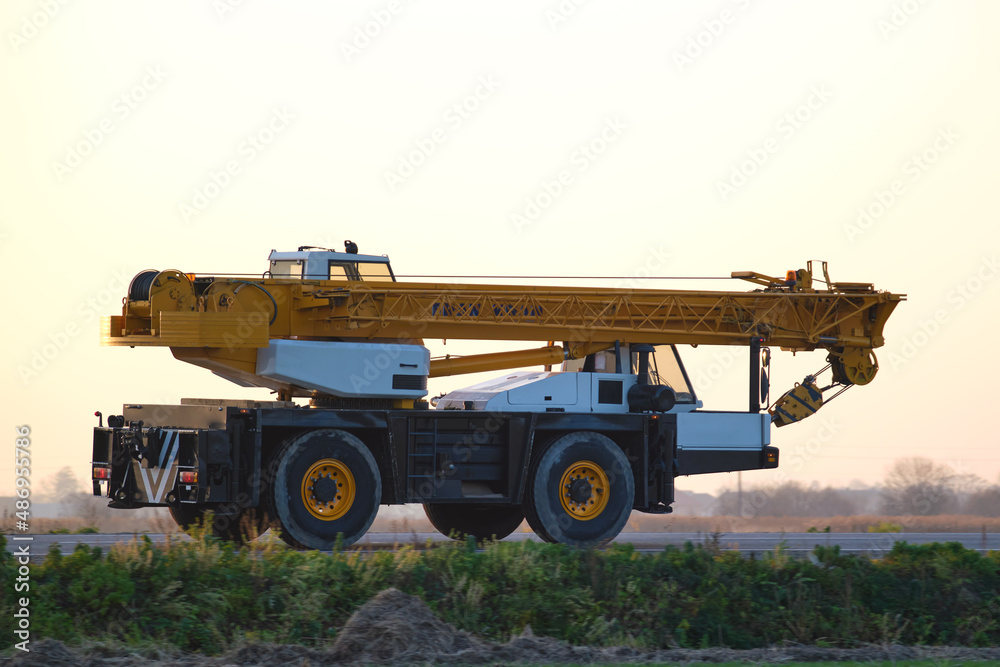 Heavy duty mobile lifting crane driving on intercity road at sunset Heavy duty mobile lifting crane driving on intercity road at sunset