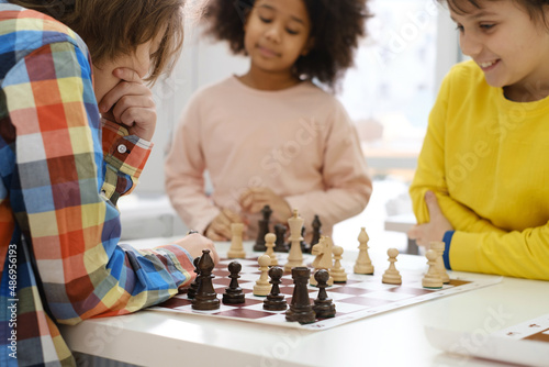 Diverse Group of kids playing chess. Concentrated multiethnic clever children with board game having fun at school. African American girl and Caucasian boys on chess lesson strategy