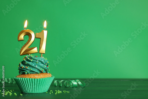 Coming of age party - 21th birthday. Delicious cupcake with number shaped candles on green wooden table, space for text photo