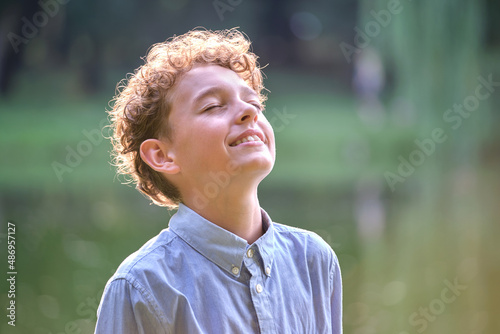 Young happy child boy relaxing in summer park. Positive kid enjoying summertime outdoors. Child wellbeing concept