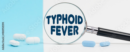 On a blue and white background, there are pills and a magnifying glass, inside of which it is written - TYPHOID FEVER