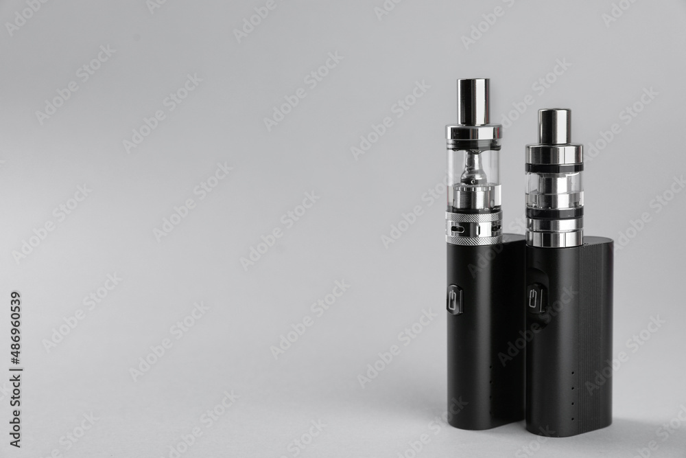 Two electronic cigarettes on light background, space for text Two electronic cigarettes on light background, space for text