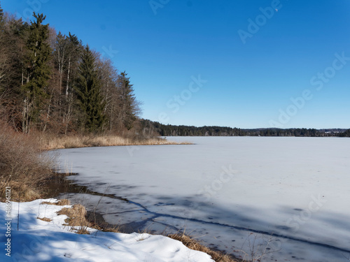 Schnee- und Eislandschaft in Oberbayern. Zugefrorener Kirchsee, kleiner Moorsee bei Sachsenkam umgeben von Buchen- und Tannenwäldern des Naturschutzgebietes bei Ellbach-Kirchseemoor