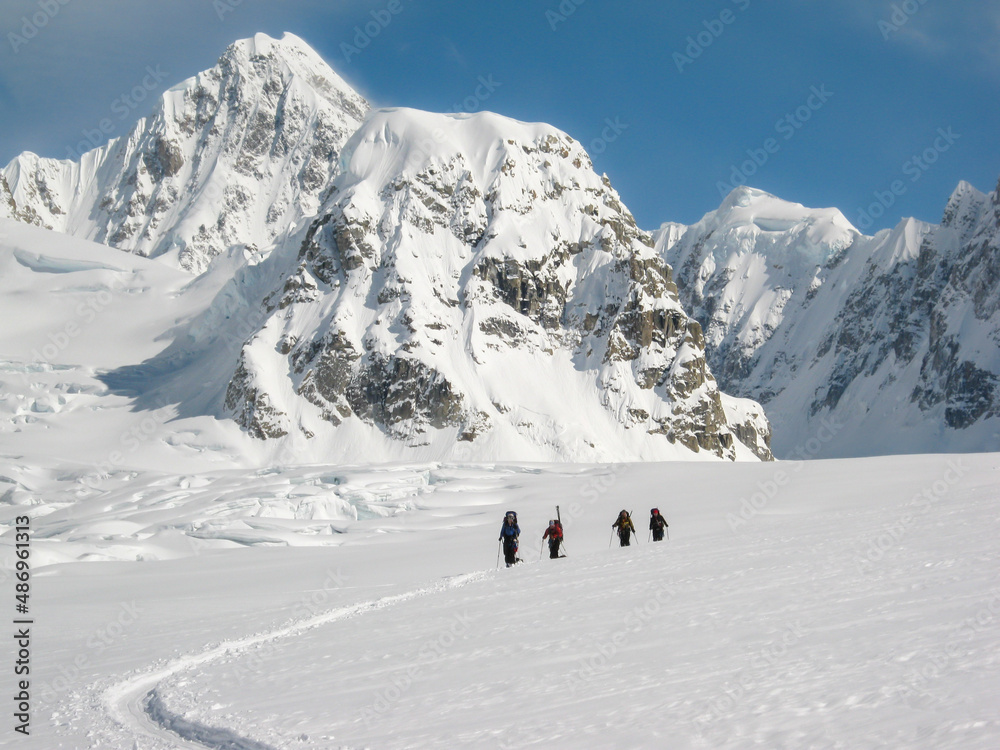 Mountaineering rope team traveling on a snowy glacier in the Alaska Range with snowcapped mountains and blue sky in the background